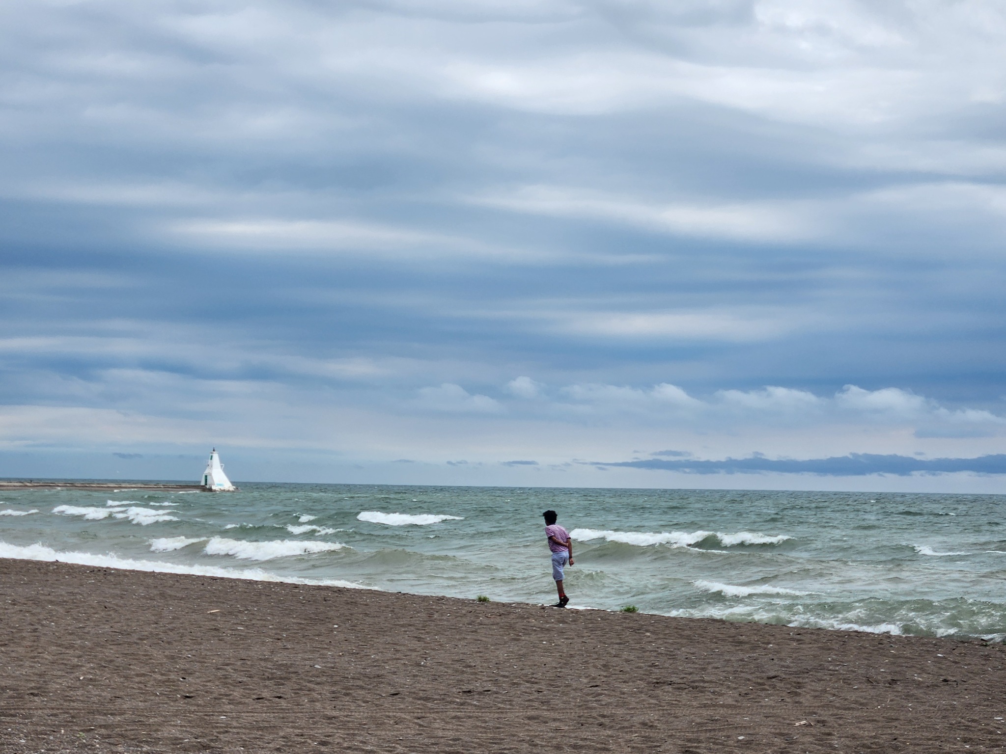 A child standing on a beach looking at waves under a dramatic sky.